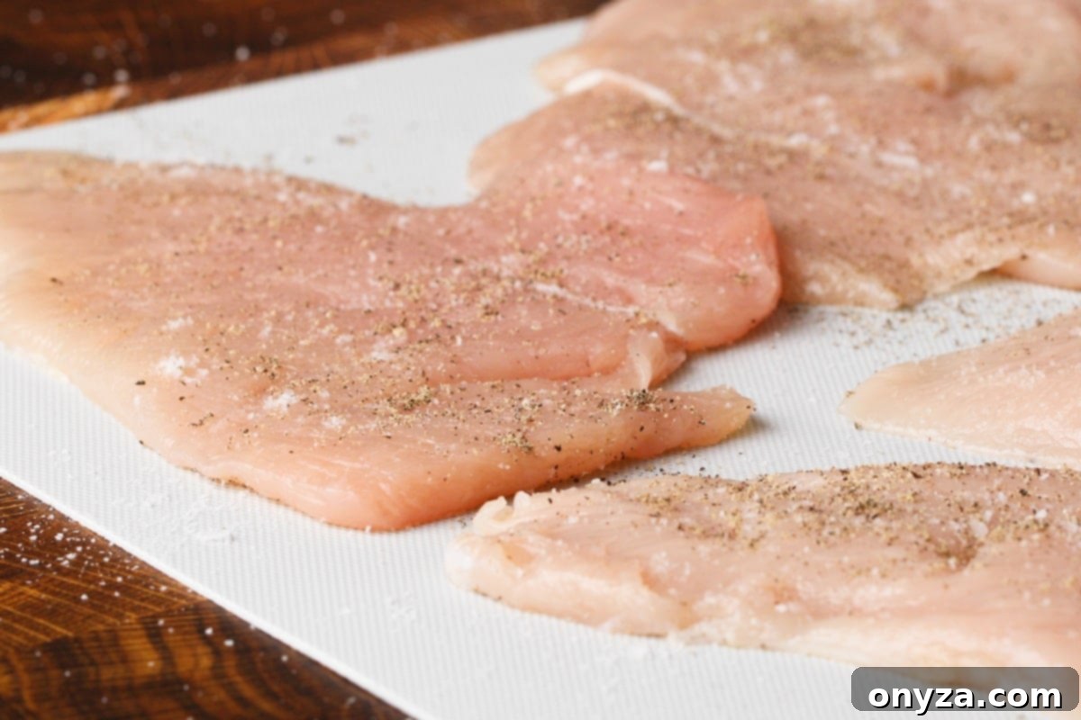 Pounded chicken cutlets, perfectly seasoned with kosher salt and freshly ground black pepper, resting on a clean white cutting board, ready for the next step.