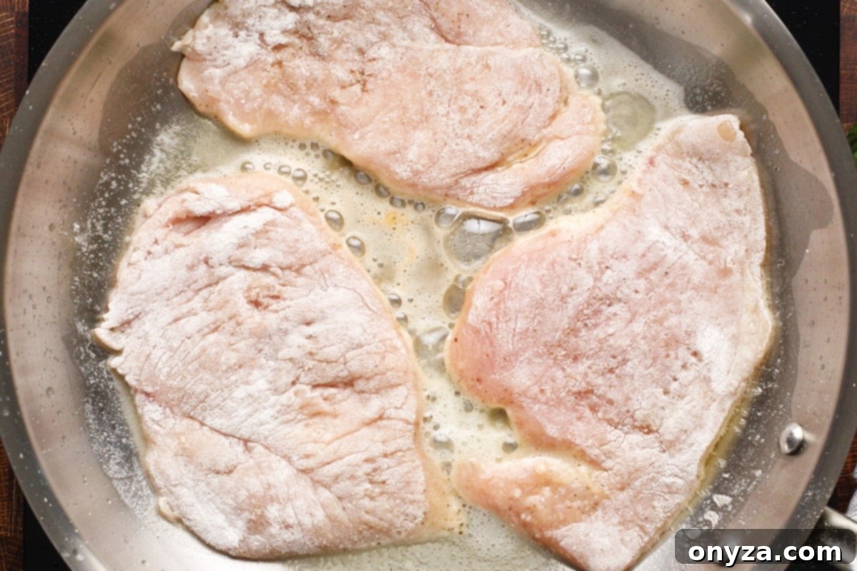 Three floured chicken cutlets sizzling in a large skillet with melted butter and olive oil, beginning to develop a golden-brown crust.