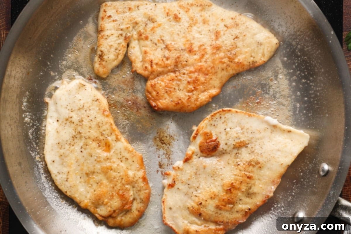 Three perfectly browned chicken cutlets resting in a stainless steel frying pan, exhibiting a beautiful golden crust.