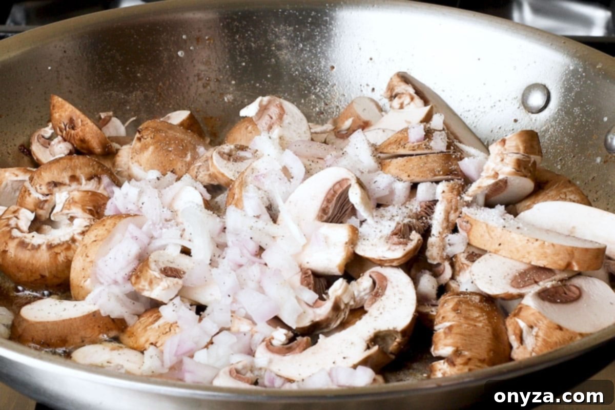 Sliced cremini mushrooms and finely chopped shallots added to a stainless steel frying pan, ready to be sautéed until golden.