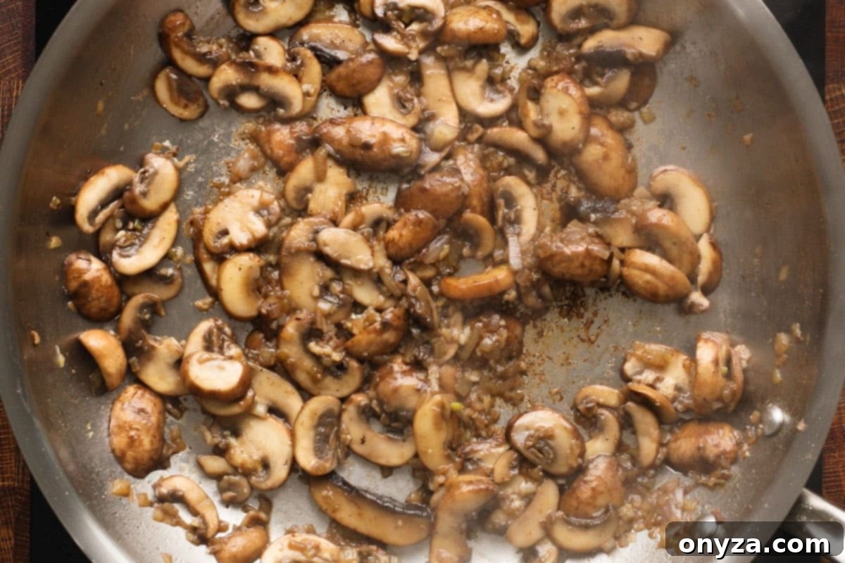Expertly sautéed mushrooms, shallots, and garlic, cooked to perfection in a stainless steel frying pan, ready to be removed for sauce preparation.