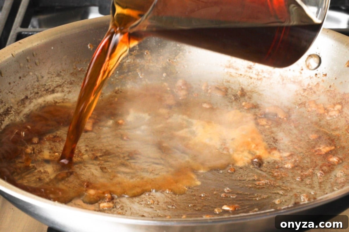 A stainless steel frying pan being deglazed with Marsala wine, as a wooden spoon scrapes up the flavorful browned bits from the bottom.