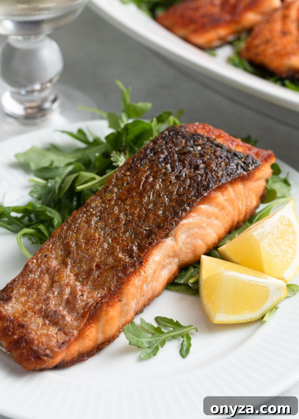 Perfectly pan seared salmon on a white plate, garnished with fresh arugula salad and vibrant lemon wedges, ready to serve.