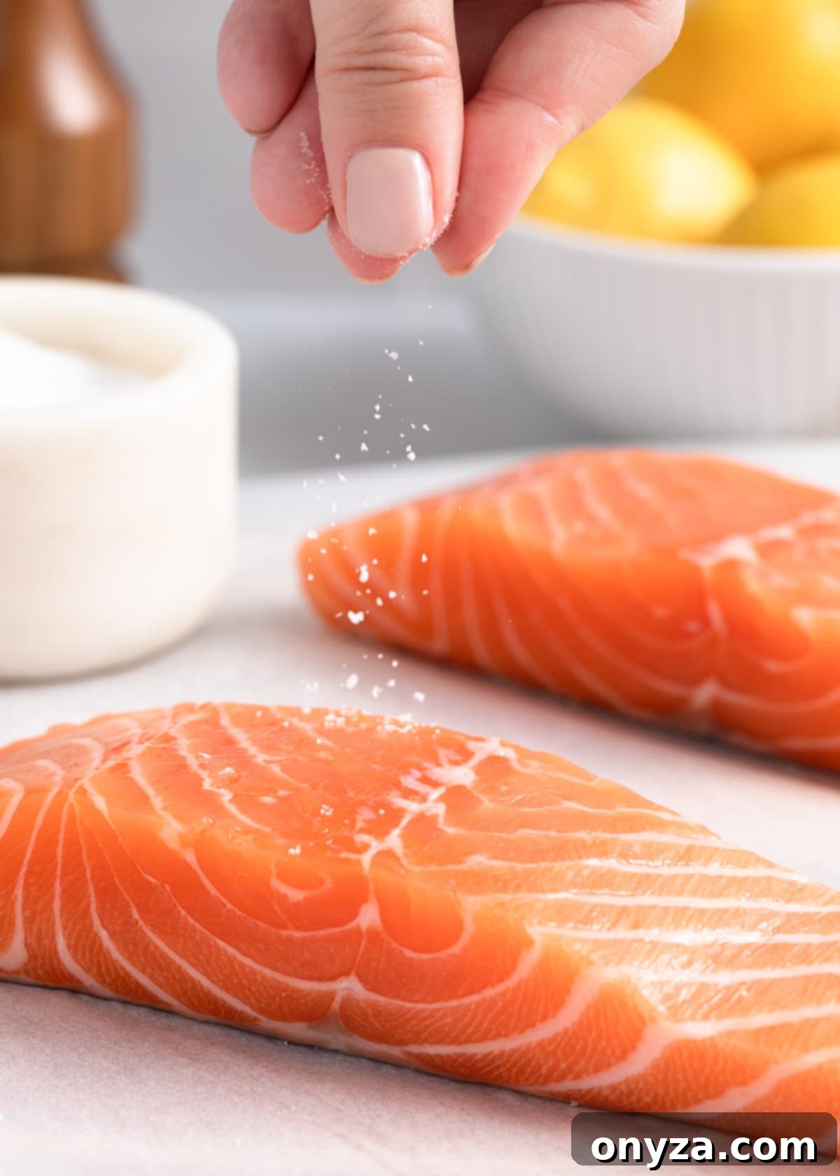 A skilled hand sprinkles kosher salt onto a raw salmon fillet, meticulously preparing it for the pan-searing process.