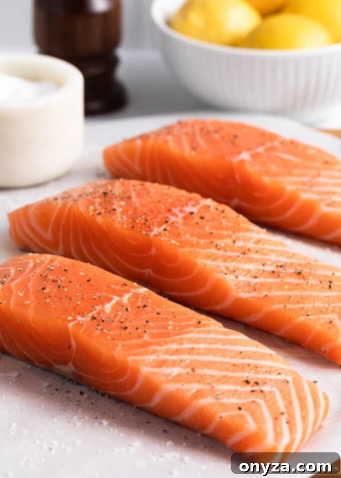 Three raw salmon fillets, meticulously seasoned with kosher salt and freshly ground black pepper, arranged on parchment paper, perfectly prepped and awaiting the pan-searing process.