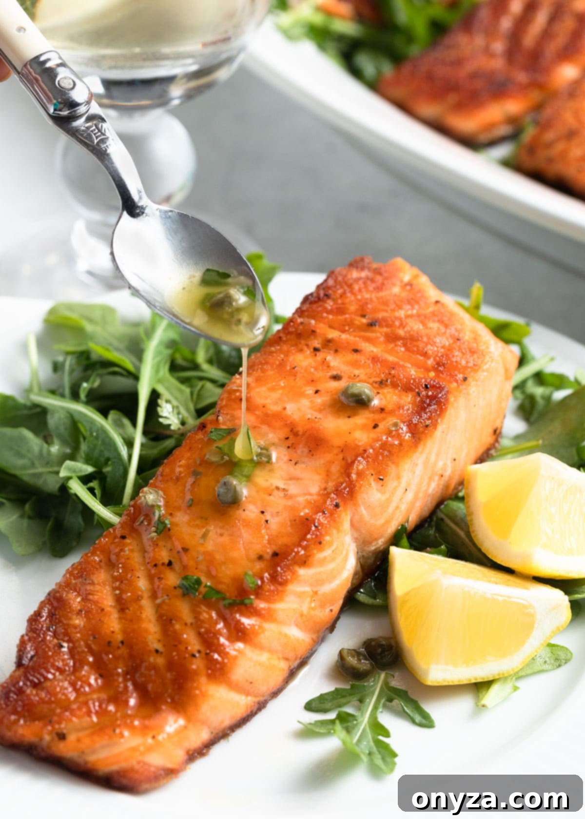 A perfectly pan-seared salmon fillet, artfully drizzled with a bright lemon caper sauce, served on a clean white plate with a sprig of fresh herbs, showcasing its restaurant-quality presentation.