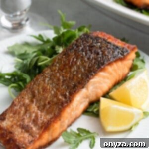 Pan-seared salmon on a white plate with arugula salad and lemon wedges