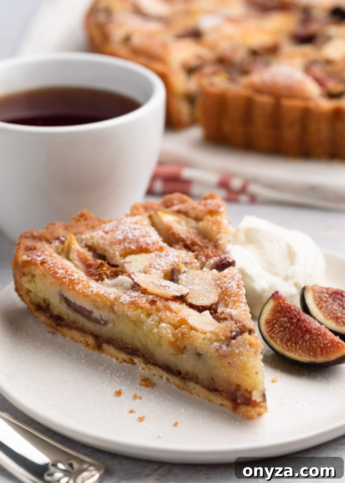 slice of fig and almond cream tart on a white plate with honey whipped cream and fresh sliced figs