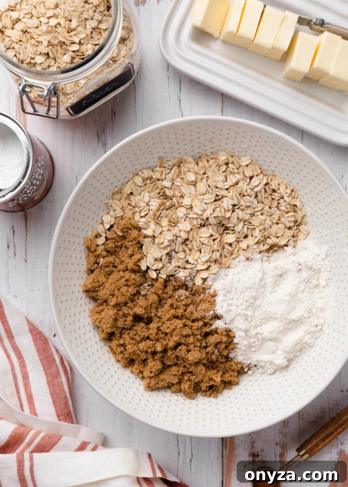 An overhead shot of a large mixing bowl filled with the dry ingredients for apple crisp topping: oats, flour, brown sugar, and spices, awaiting the addition of butter.