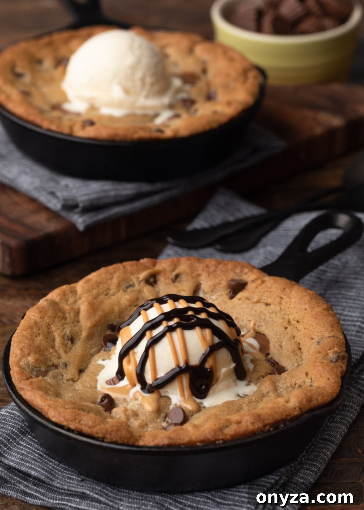 two peanut butter skillet cookies topped with vanilla ice cream; one with drizzles of peanut butter and chocolate sauces