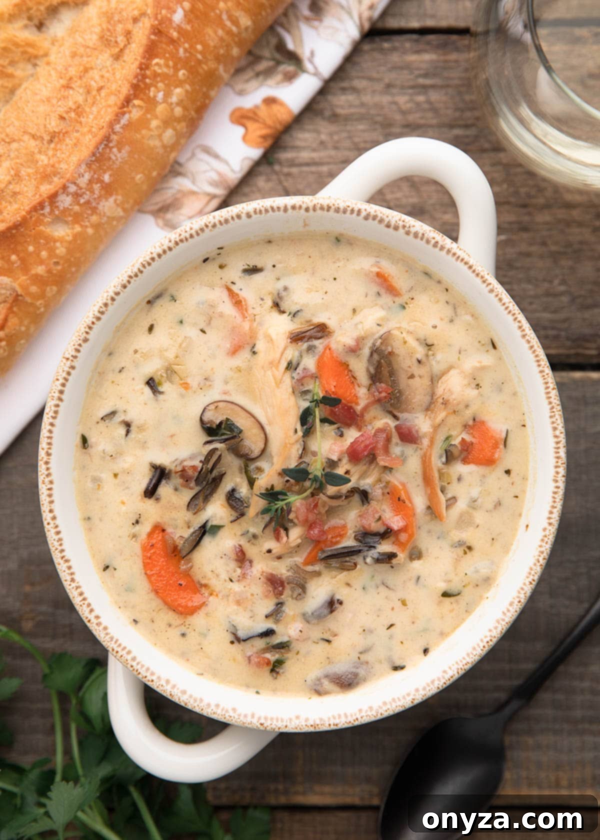 overhead photo of cream of turkey wild rice soup on a wood board next to a baguette
