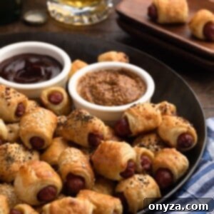 puff pastry pigs in a blanket on a bronze serving platter with bowls of grainy mustard and bbq sauce