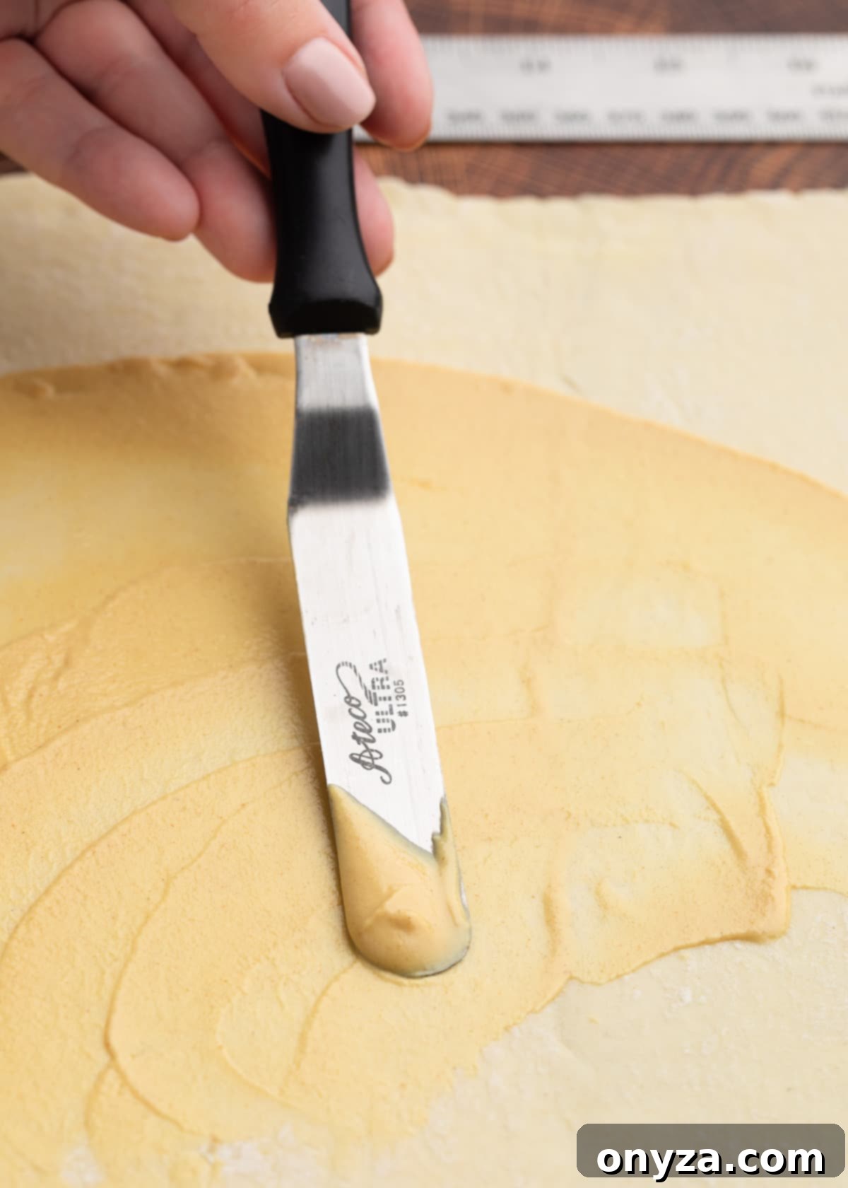 Spreading Dijon mustard onto puff pastry with an offset spatula for pigs in a blanket