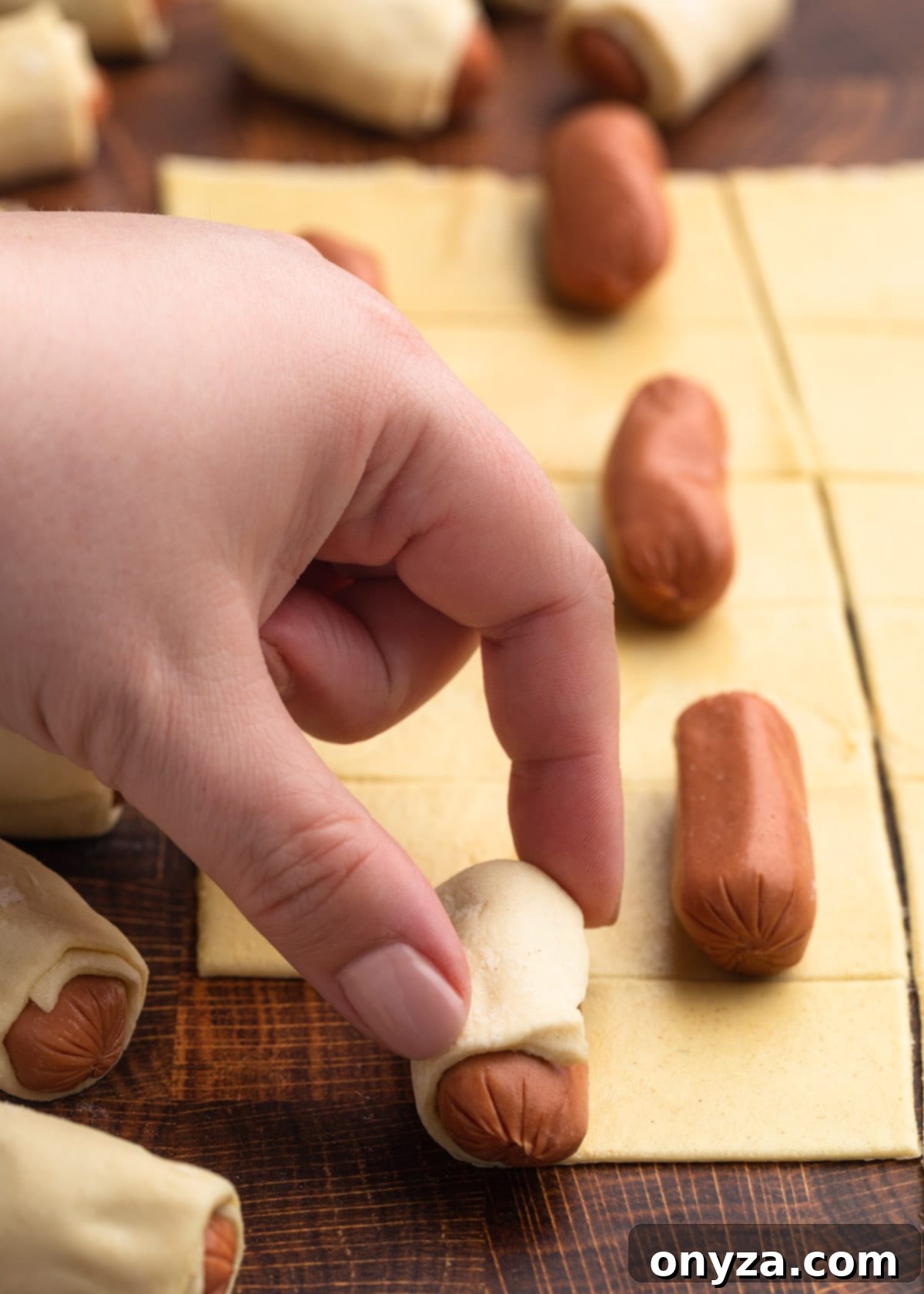 Rolling puff pastry strips around cocktail franks to make pigs in a blanket