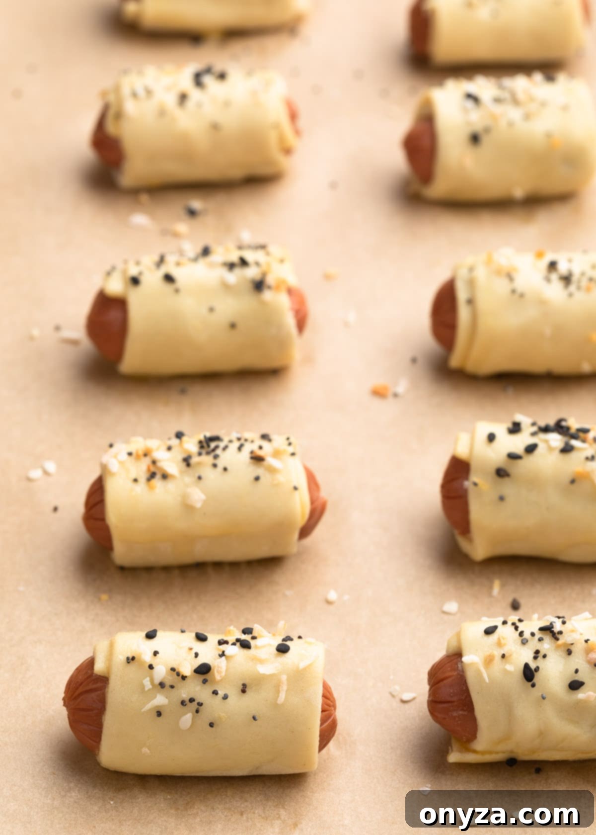 Unbaked pigs in a blanket sprinkled with everything bagel seasoning on a parchment lined baking sheet