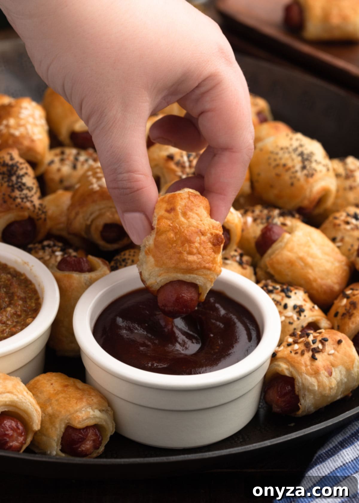 Dipping a plain puff pastry pig in a blanket into barbecue sauce