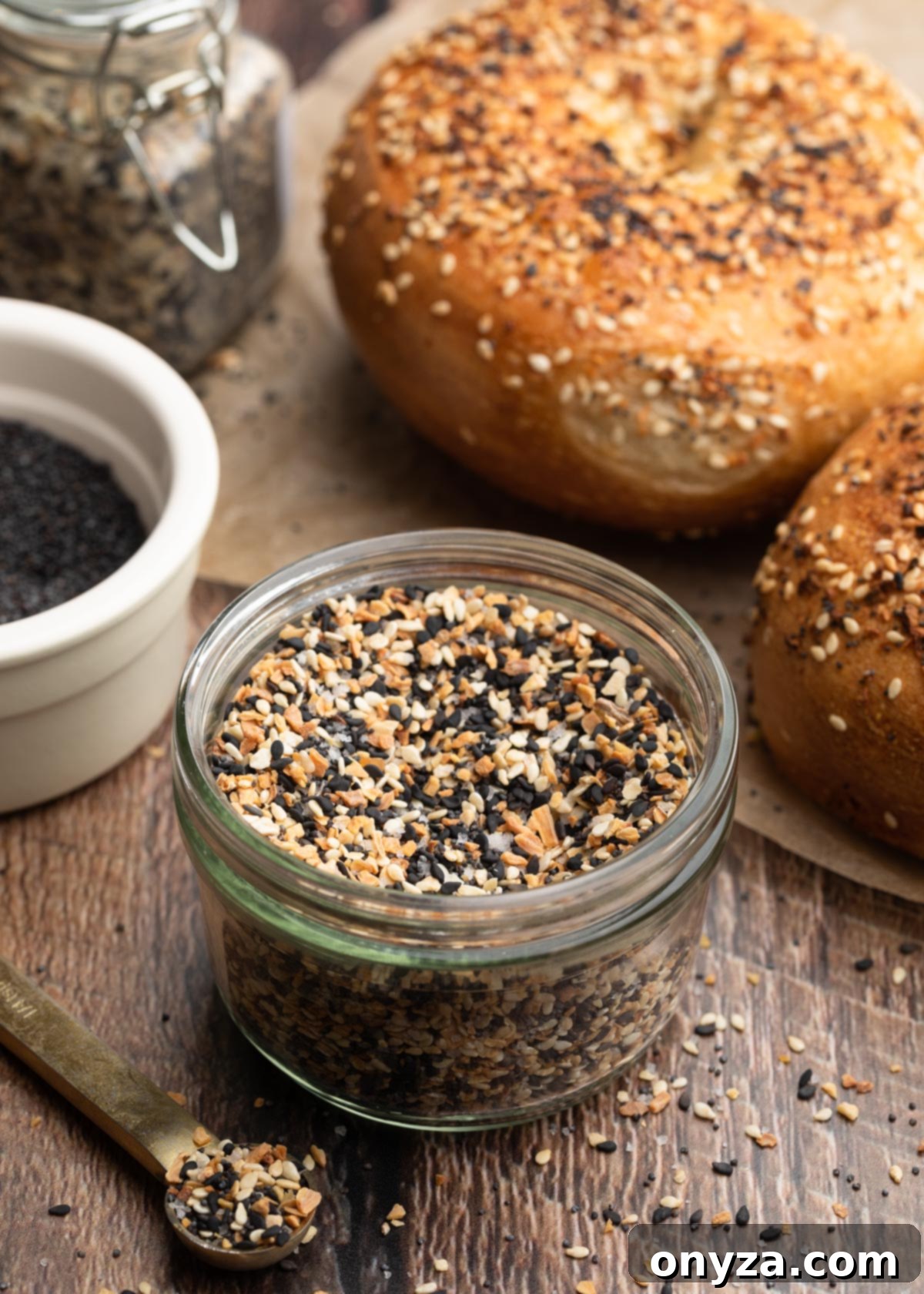 Ultimate Everything Seasoning 2 everything bagel seasoning in a glass jar, surrounded by everything bagels on a wood board