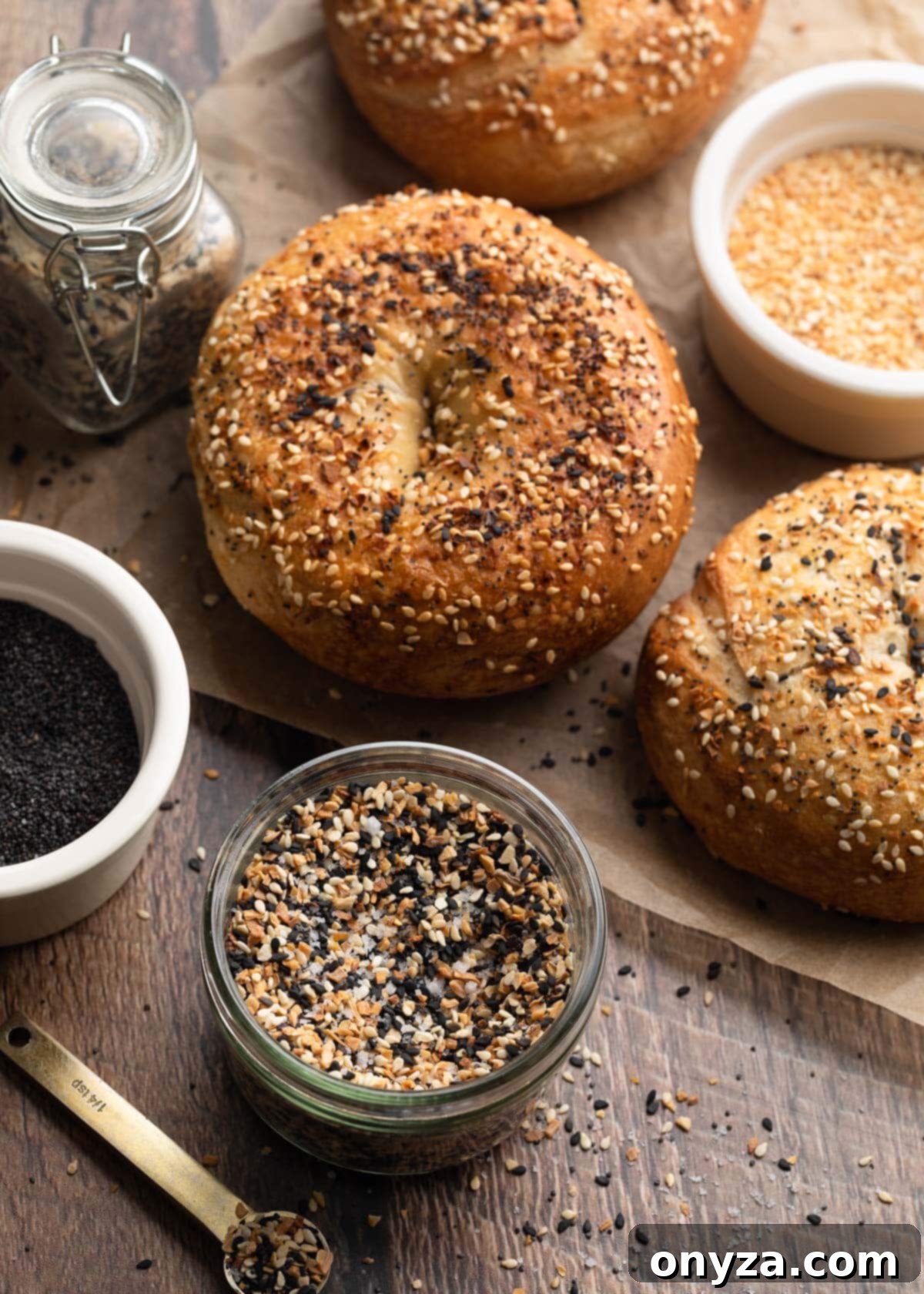 Ultimate Everything Seasoning 7 everything bagel seasoning in a jar with bowls of poppy seeds, minced dried garlic, and bagels