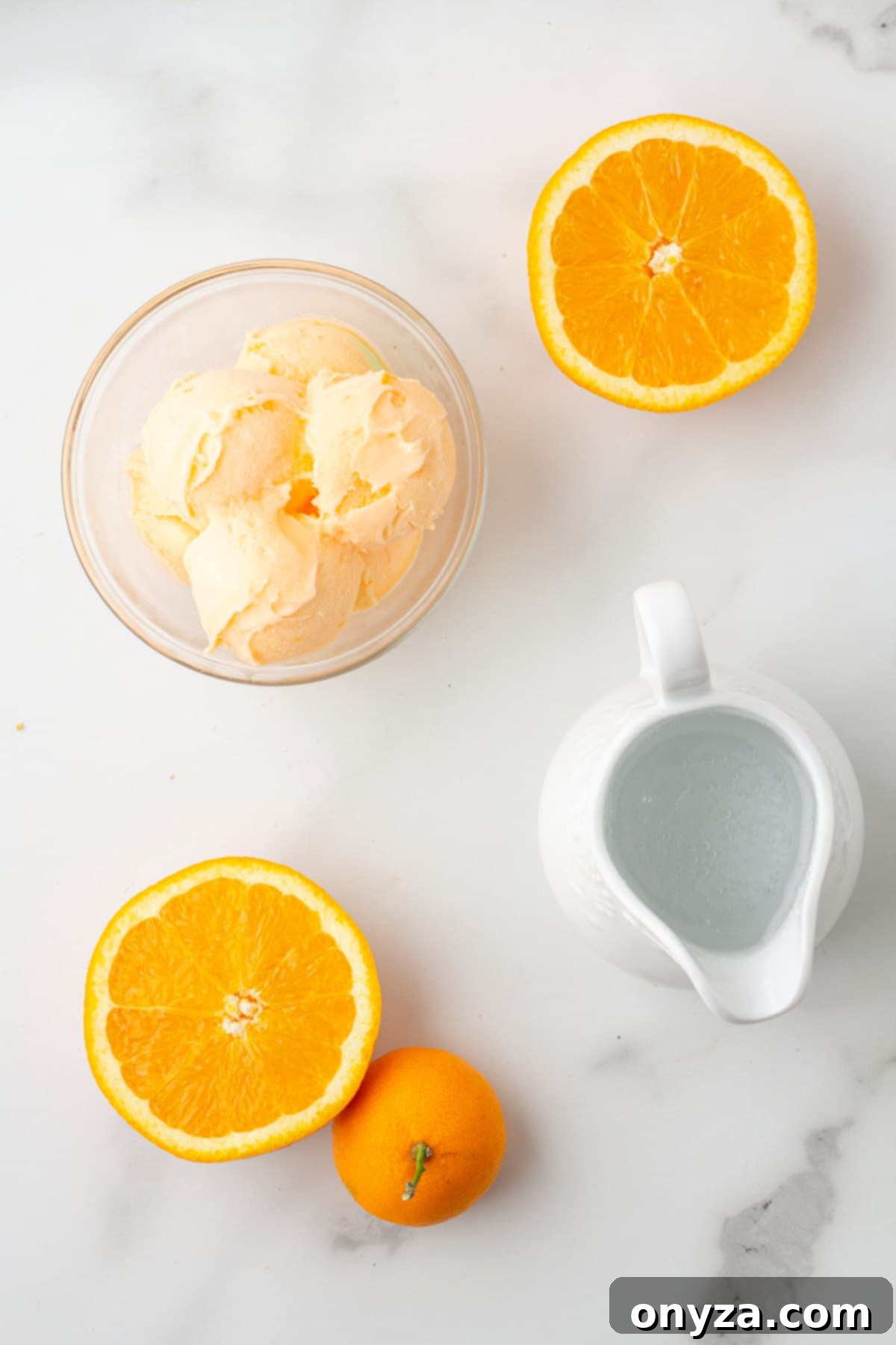 overhead photo of a bowl of orange sherbet, orange halves, and a pitcher of sparkling water