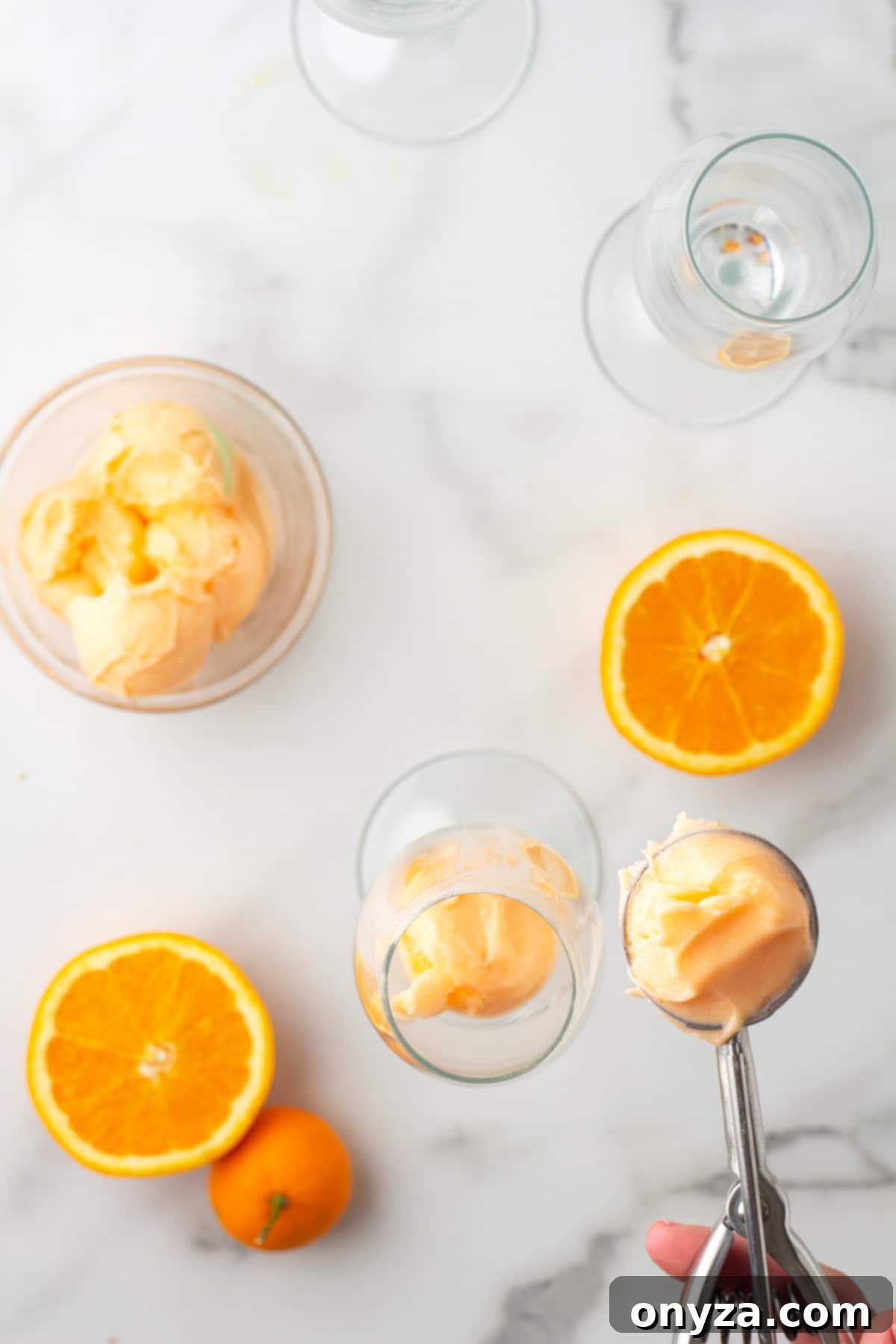 overhead view of scooping orange sherbet into a champagne glass with an ice cream scoop