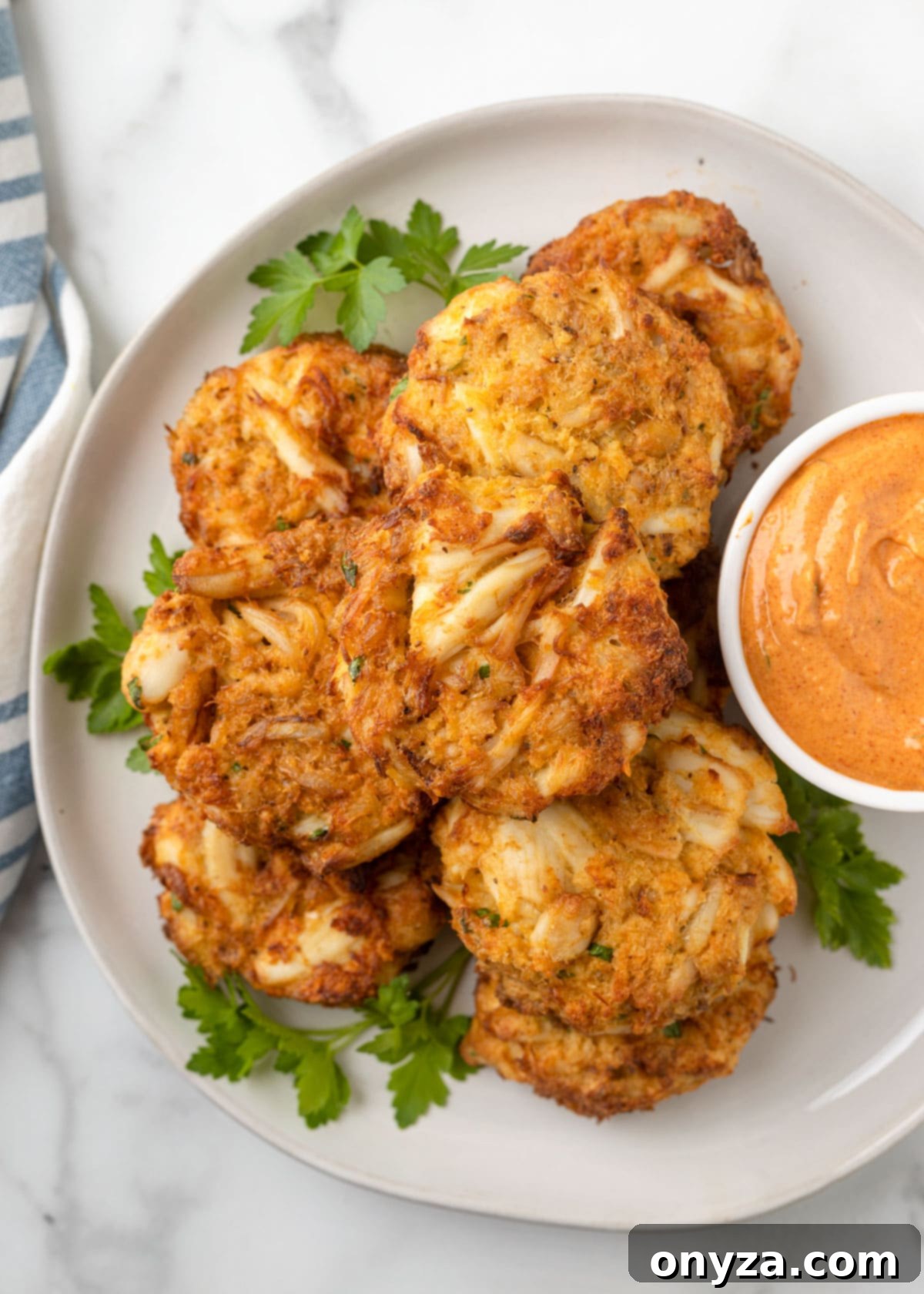 Overhead photo of three air fried crab cakes on a white plate with a small bowl of creamy remoulade sauce.