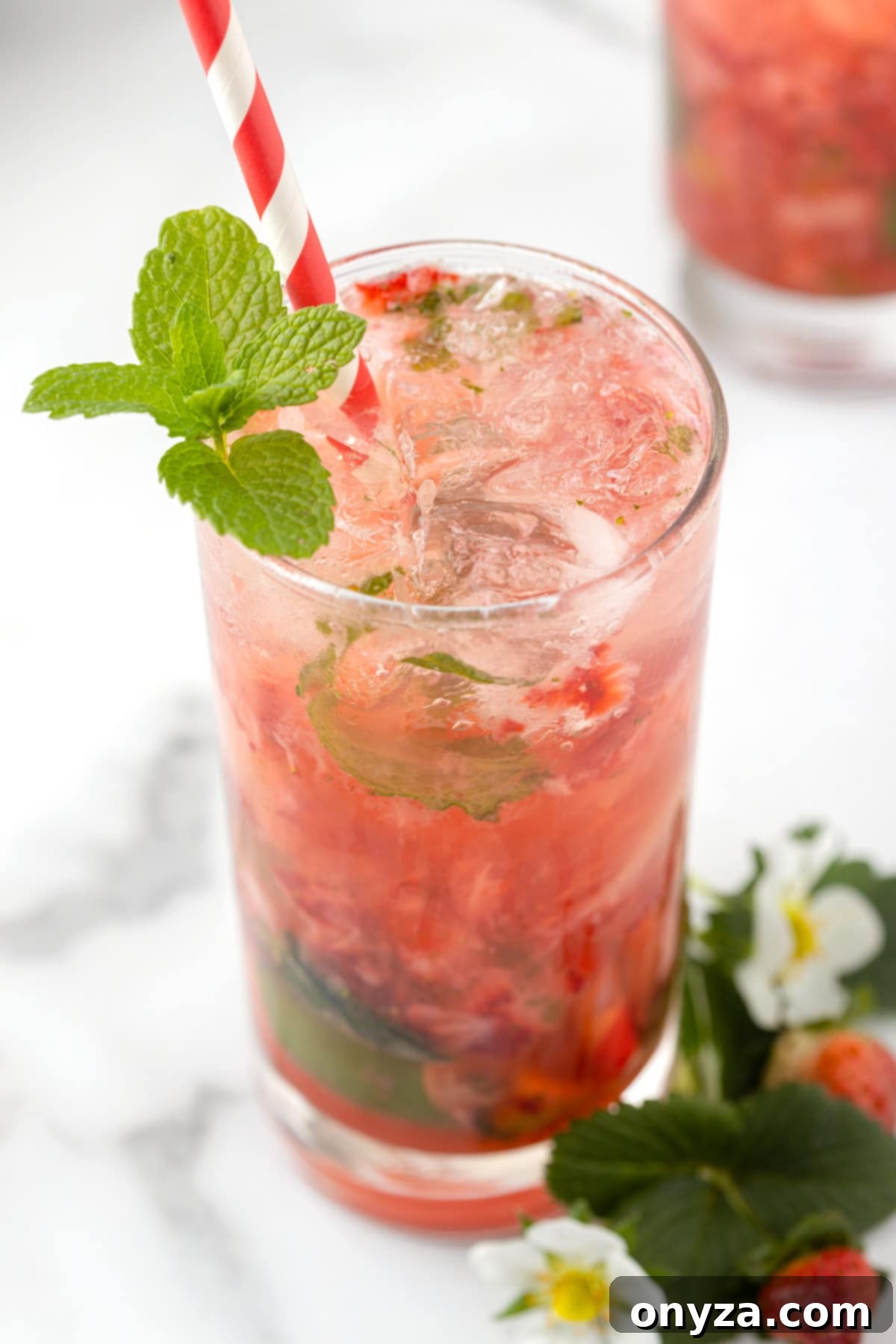Closeup of a single perfectly crafted Strawberry Mojito in a highball glass, garnished with a vibrant sprig of fresh mint and a strawberry slice, showcasing its rich red color and inviting bubbles.