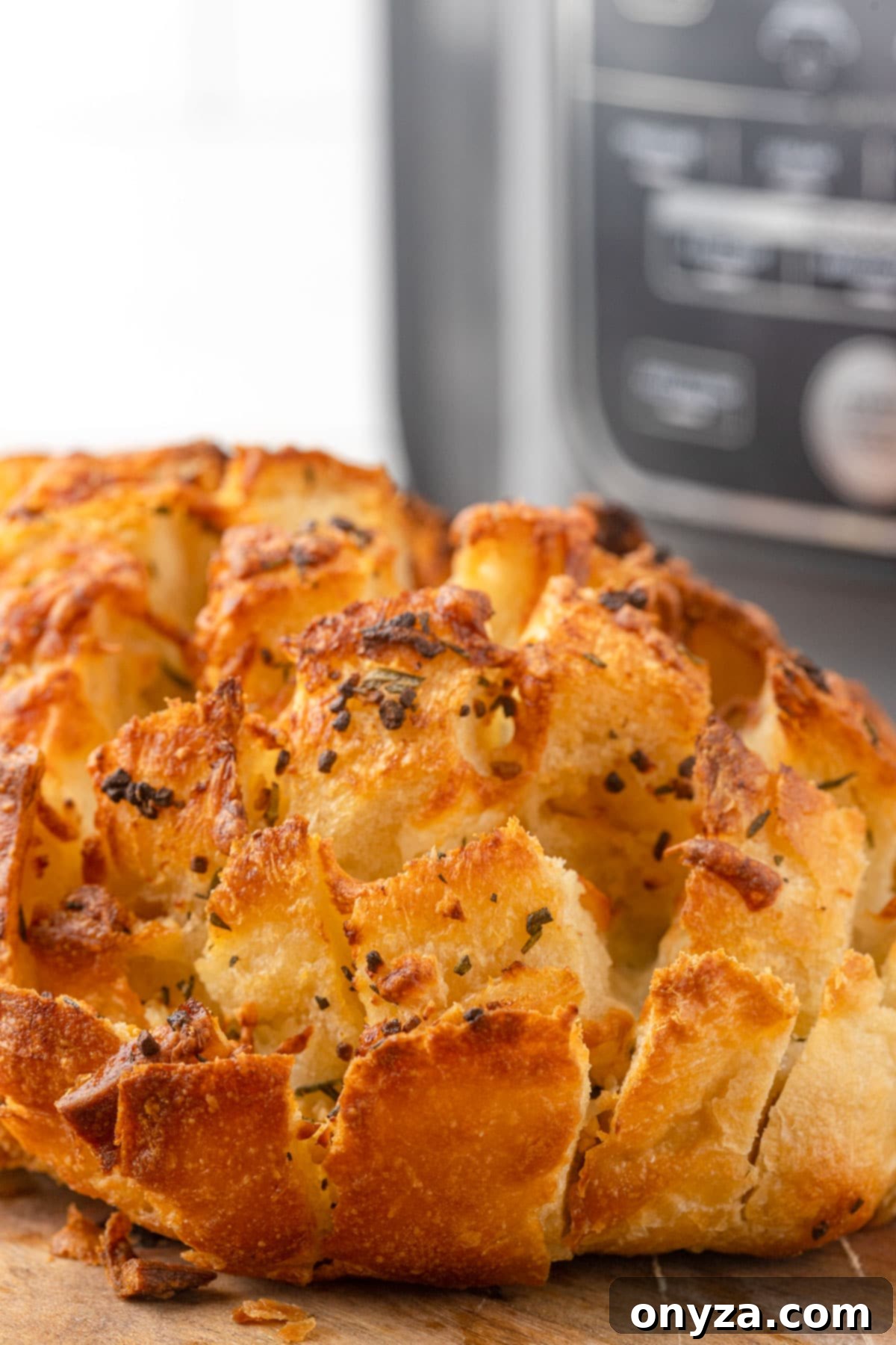 mozzarella and garlic butter pull apart bread on a wooden board in front of a ninja foodi air fryer