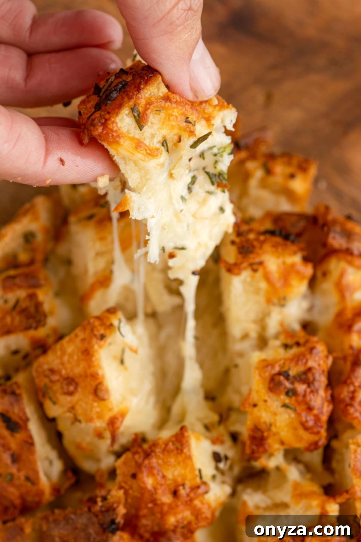 pulling a piece of garlic pull apart bread with melted mozzarella from the baked loaf, showing the gooey cheese