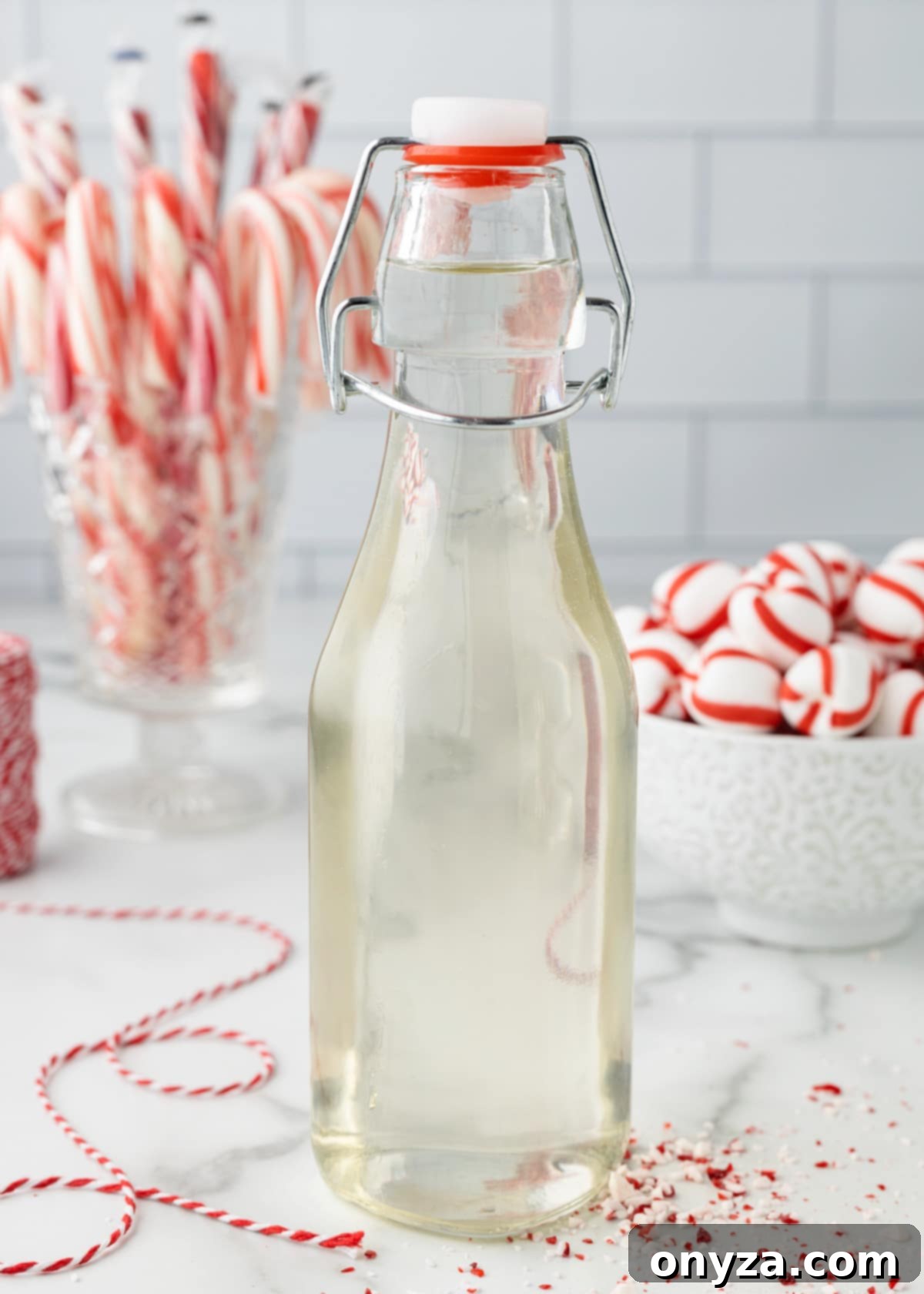 Homemade peppermint syrup in a glass bottle, surrounded by candy canes and scattered peppermint candies, evoking a festive holiday mood.