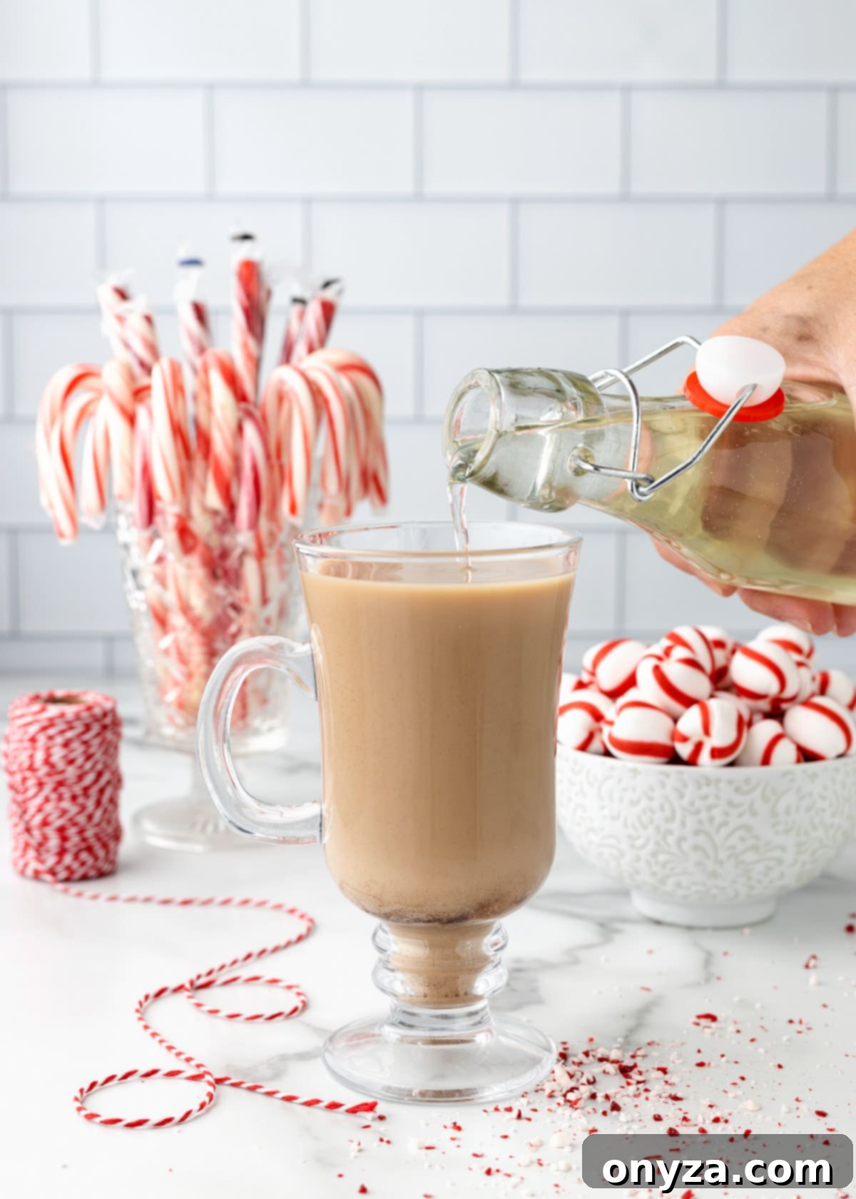Peppermint syrup being generously poured into a hot coffee drink in a clear glass mug, ready to be enjoyed.