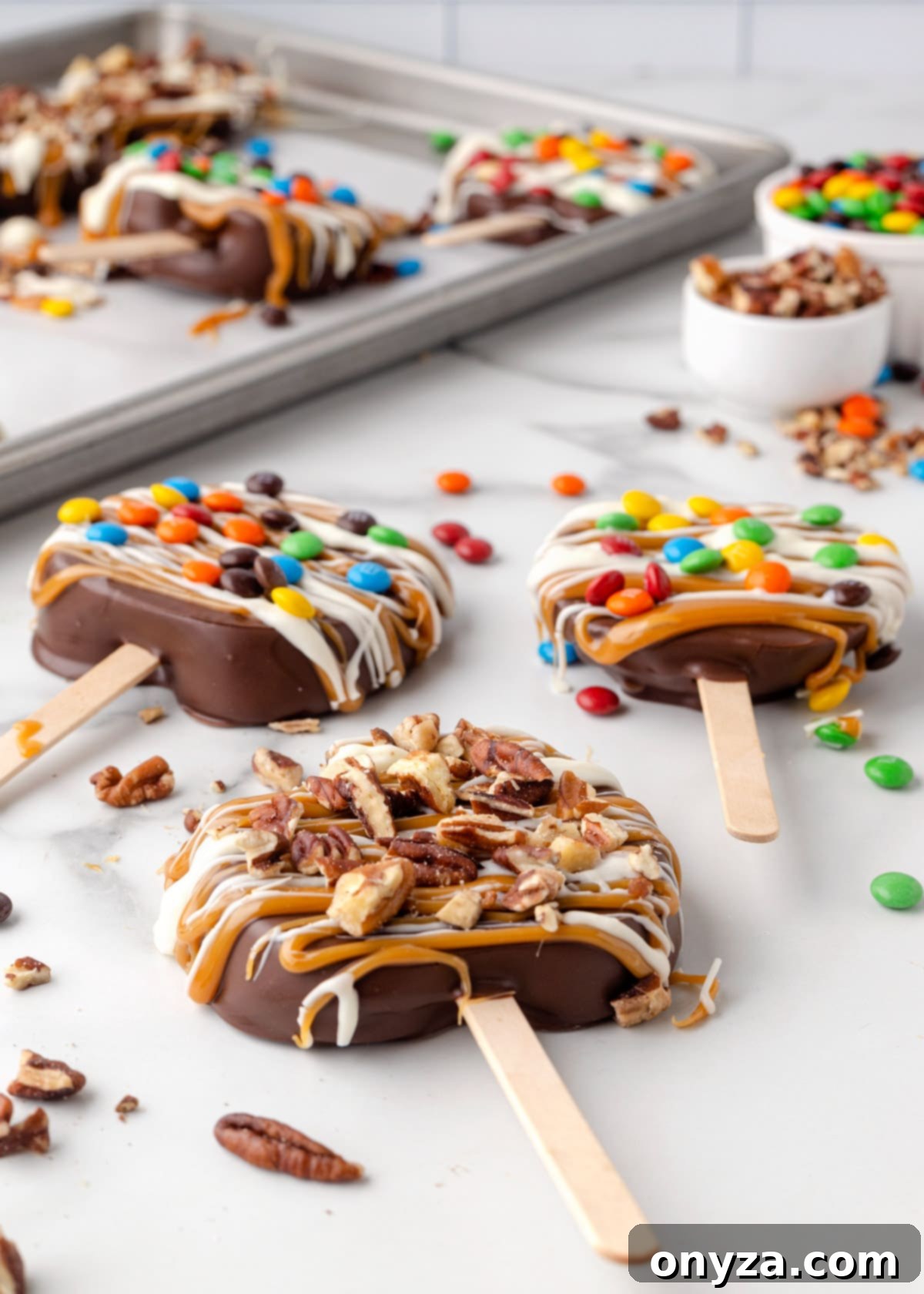 chocolate covered caramel apple slices decorated with candies and nuts on a white marble countertop