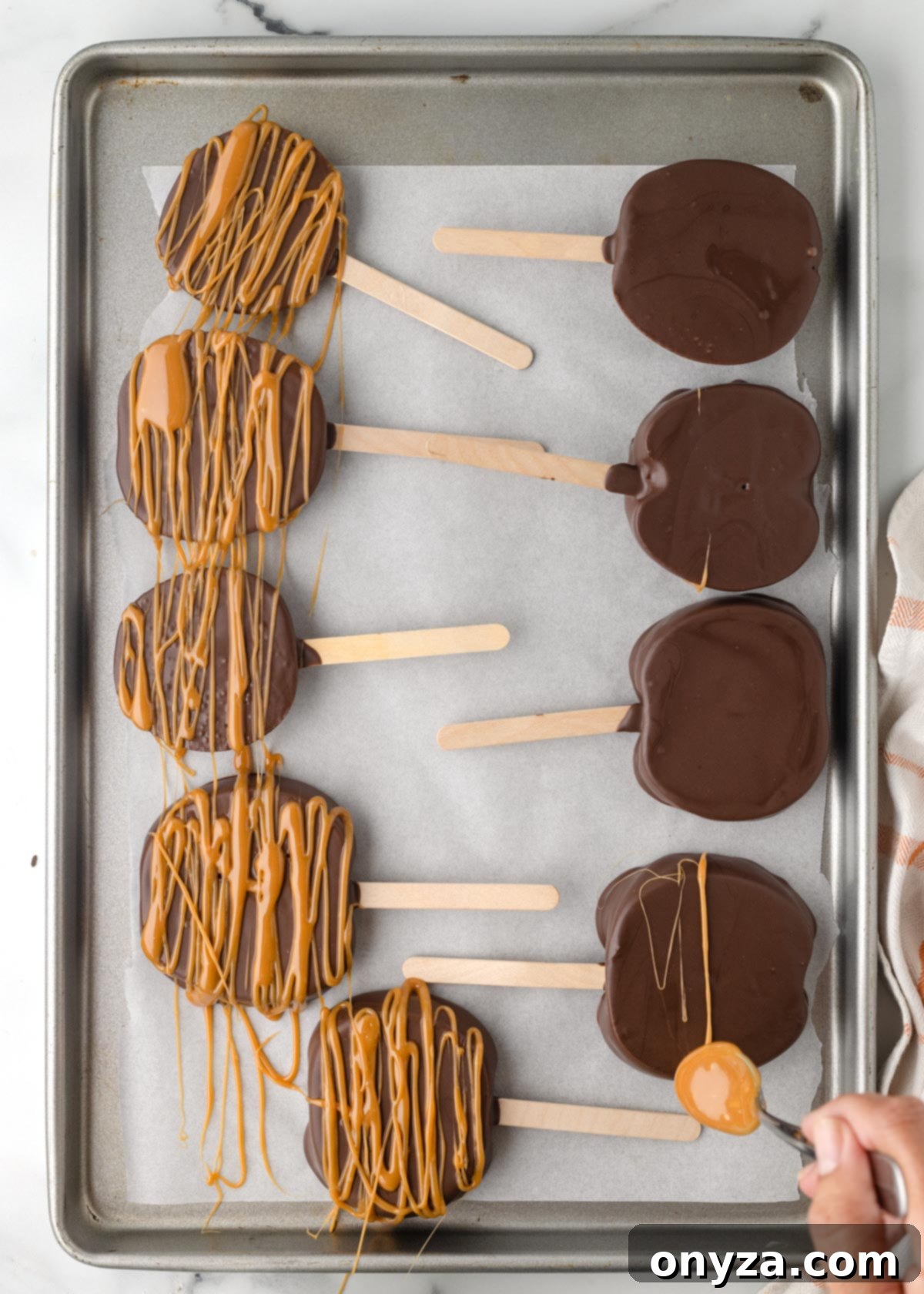 drizzling caramel over chocolate covered apple slices on a parchment lined baking sheet