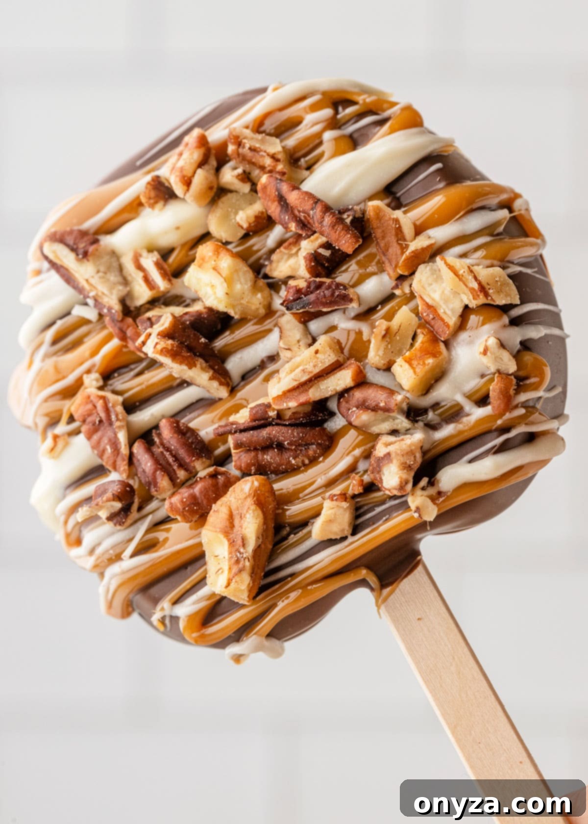 caramel apple slice on a popsicle stick with white chocolate drizzle and pecans