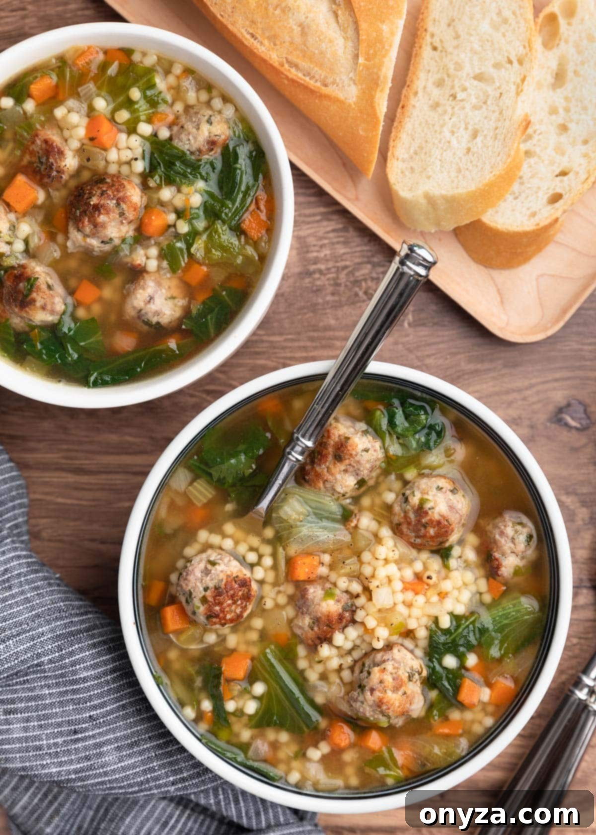 Overhead photo of two bowls of Italian Wedding Soup, ready to be served, on a wooden background with a sliced loaf of Italian bread.