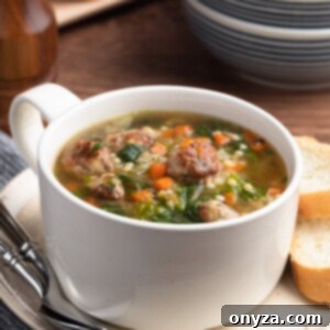 Italian Wedding Soup in a white handled bowl on an ivory ceramic plate with two spoons and slices of Italian bread