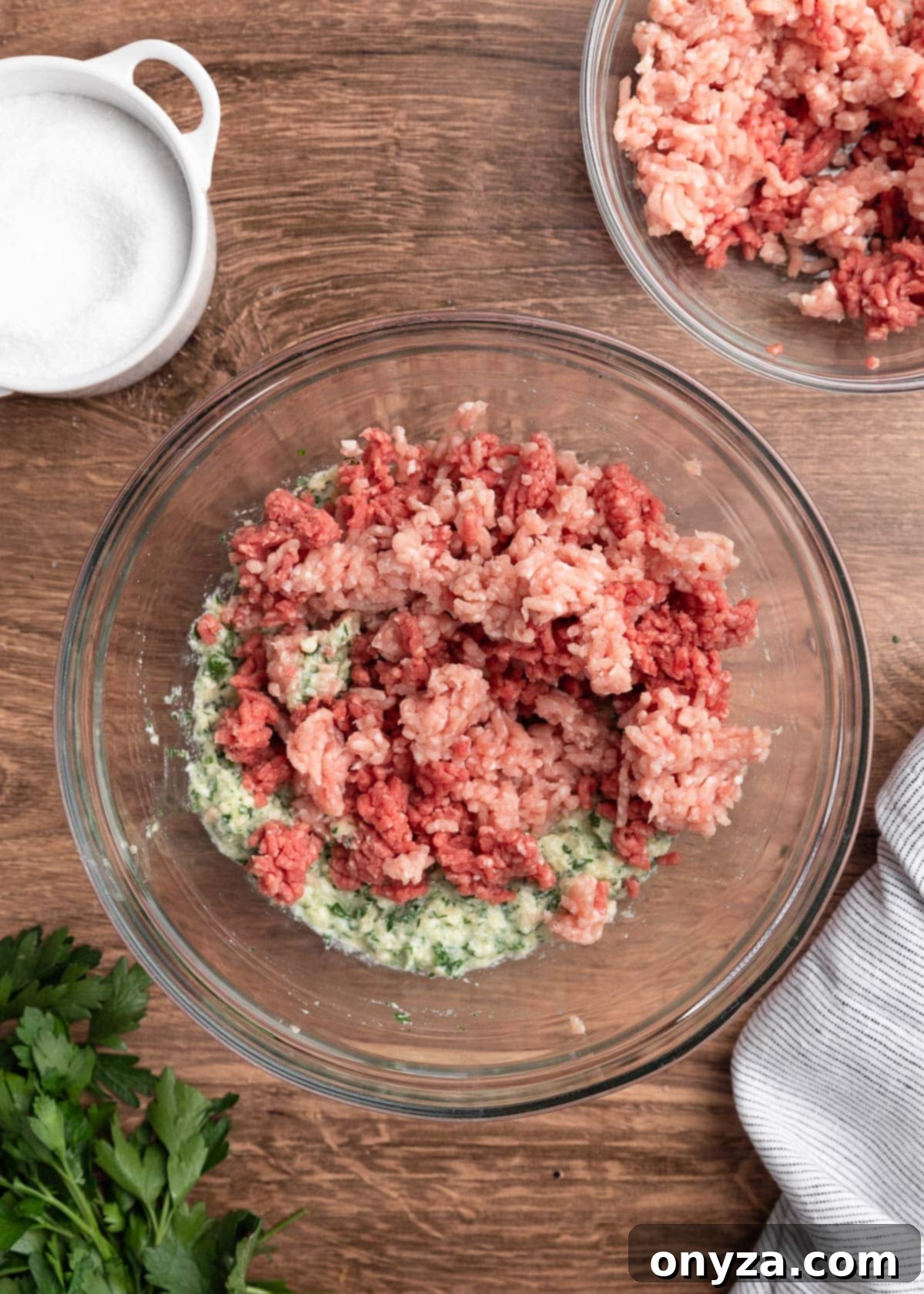 Ground beef and pork in a glass bowl, ready to be mixed with the seasoned panade on a wooden board.