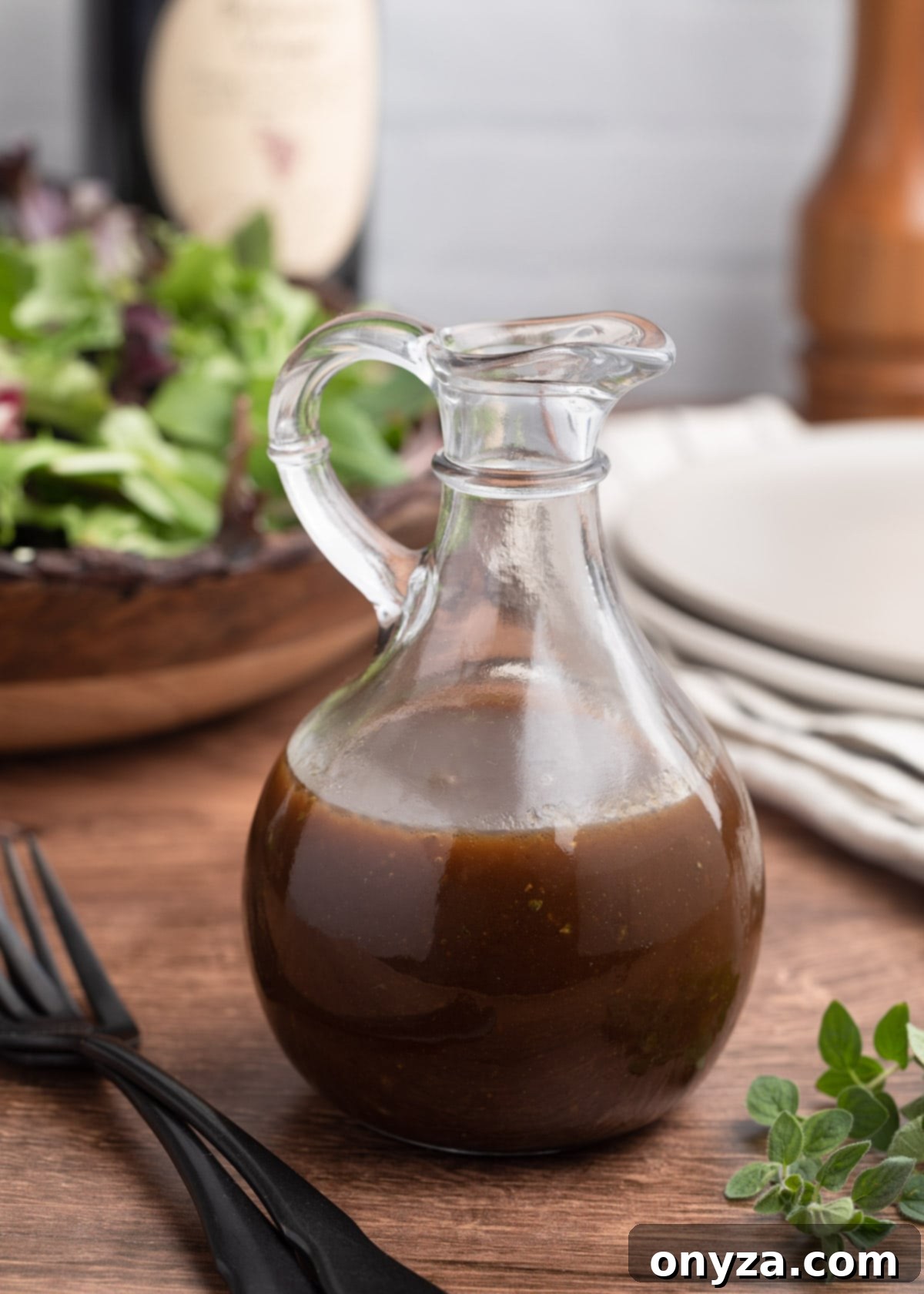 Tangy Balsamic Dressing 2 A beautiful glass cruet filled with golden-brown homemade balsamic vinaigrette, ready to pour. It stands prominently in front of a rustic wooden bowl brimming with fresh, crisp spring mix lettuce, hinting at a delicious, healthy meal.