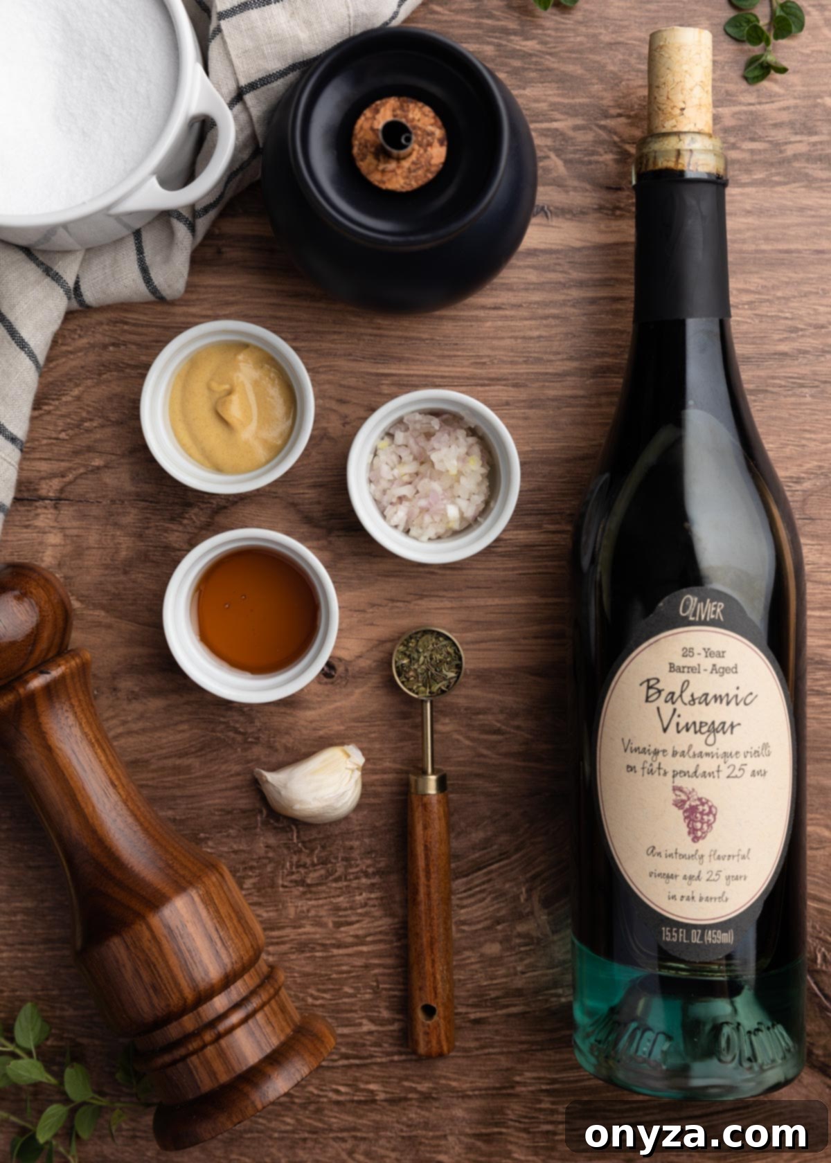 Tangy Balsamic Dressing 3 An overhead view capturing the essential ingredients for homemade balsamic vinaigrette. A bottle of premium balsamic vinegar is featured alongside small pinch bowls holding extra virgin olive oil, minced shallots, garlic, Dijon mustard, honey, and dried herbs, all laid out on a clean surface.