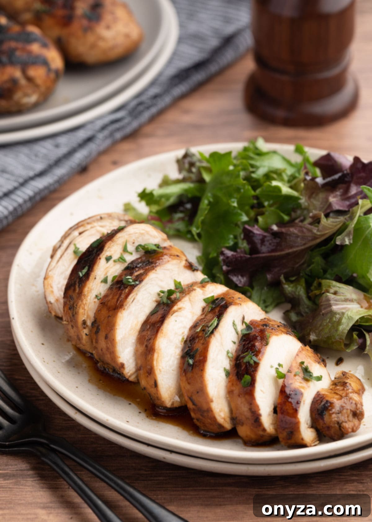 Sliced balsamic marinated chicken breast on an ivory plate with a fresh green salad