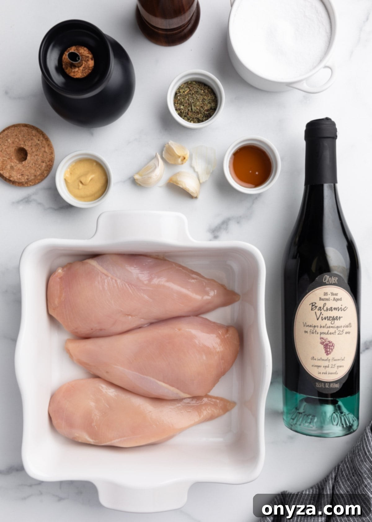 Overhead photo of boneless skinless chicken breasts in a white baking dish, surrounded by a bottle of balsamic vinegar and marinade ingredients in small bowls