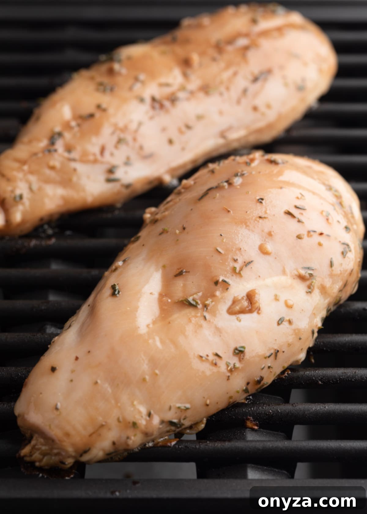 Two raw balsamic marinated chicken breasts on grill grates