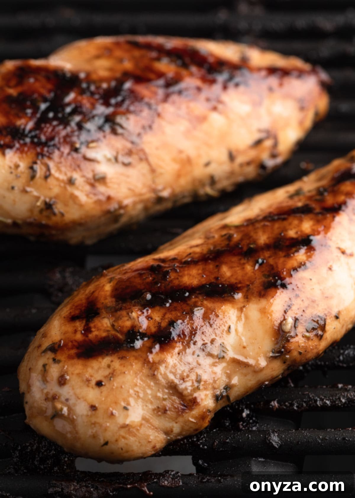 Two cooked balsamic marinated chicken breasts on grill grates