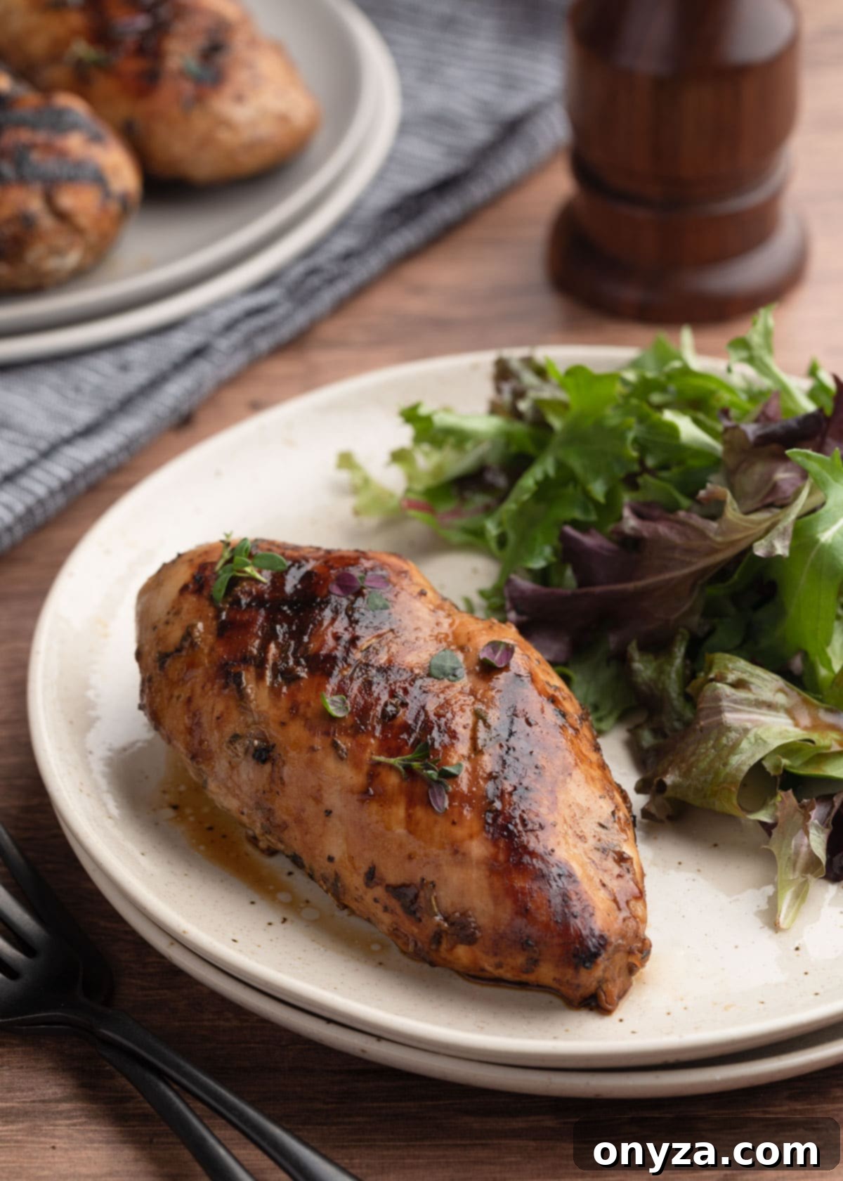 Whole grilled balsamic chicken breast on an ivory plate with spring greens