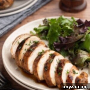 Sliced balsamic marinated chicken breast on an ivory plate with a green salad