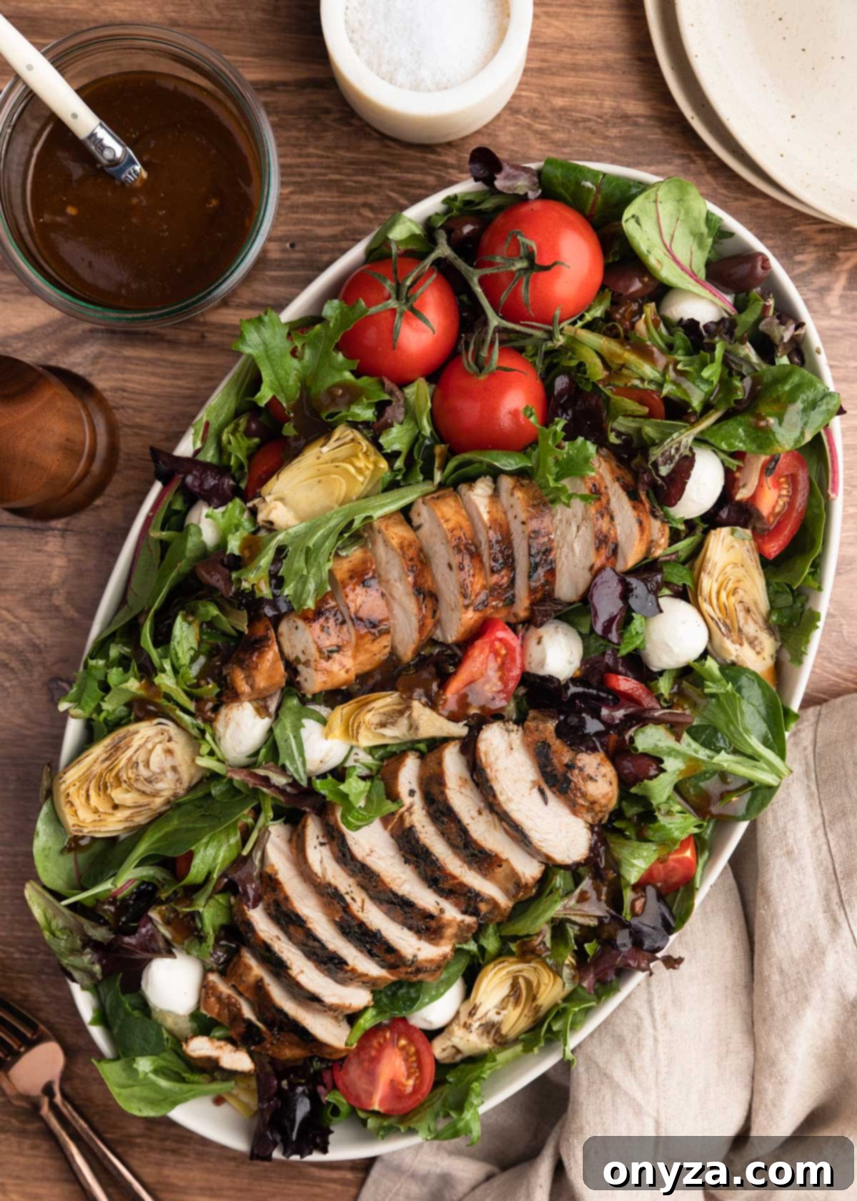 overhead photo of balsamic grilled chicken salad in a white over platter on a wood background