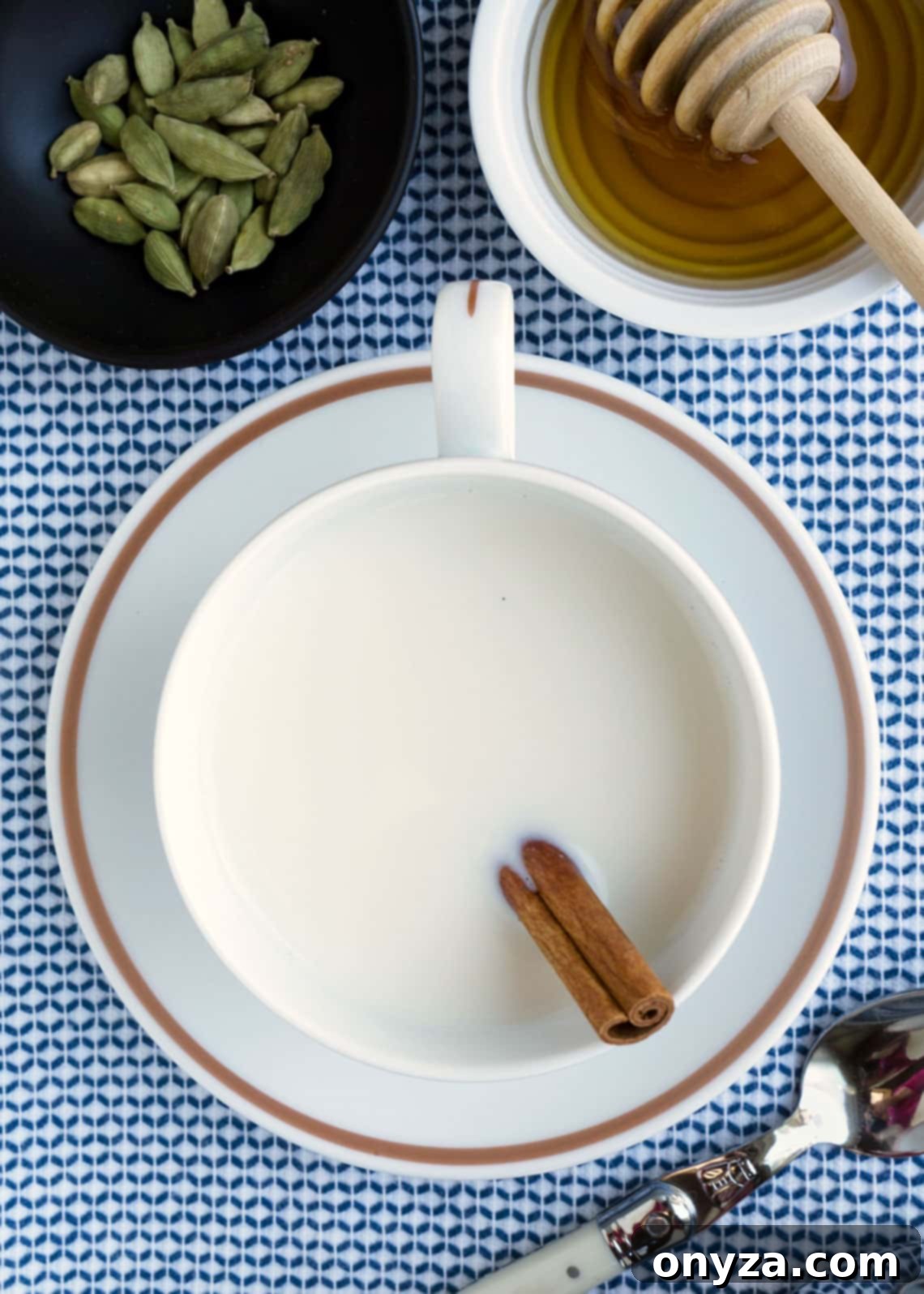 Overhead photo of a steaming teacup of cardamom-spiced milk, garnished with a cinnamon stick, resting on a serene blue and white napkin, inviting a moment of calm and warmth.