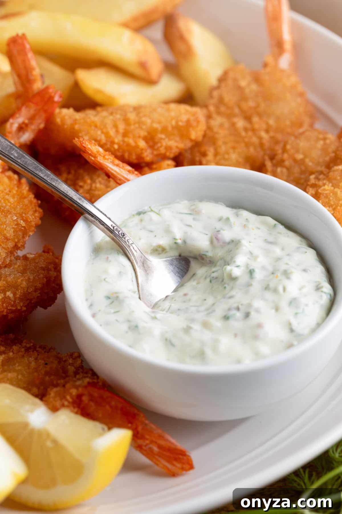 A crisp white bowl overflowing with homemade tangy tartar sauce, elegantly placed on a rustic wooden platter alongside a generous serving of golden-fried shrimp and perfectly cooked french fries. A silver spoon rests in the bowl, ready for dipping.