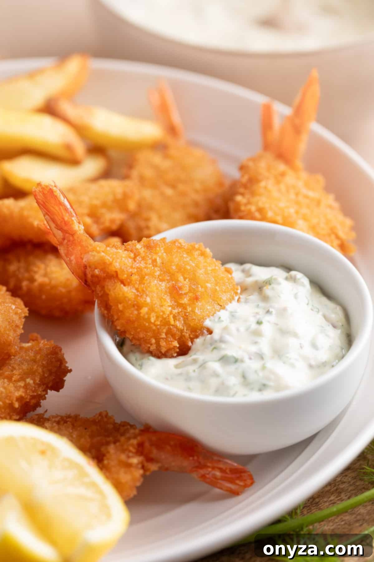 A beautifully presented platter featuring crispy, golden-brown fried breaded shrimp and perfectly seasoned french fries. A small, elegant white bowl of homemade tangy tartar sauce sits invitingly on the platter, with one shrimp already dipped into the creamy sauce, ready to be enjoyed.