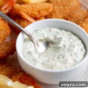Tartar Sauce in a white bowl with a silver spoon on a platter of fried shrimp and french fries