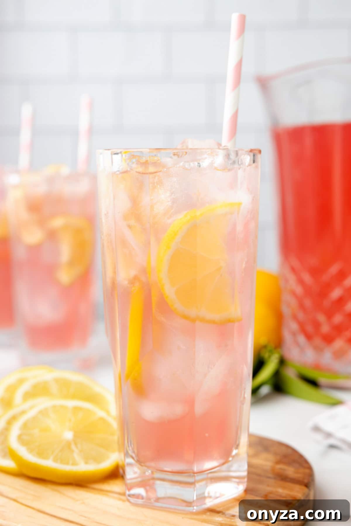 Two glasses of homemade pink lemonade garnished with lemon slices and pink striped paper straws, ready for a refreshing sip.